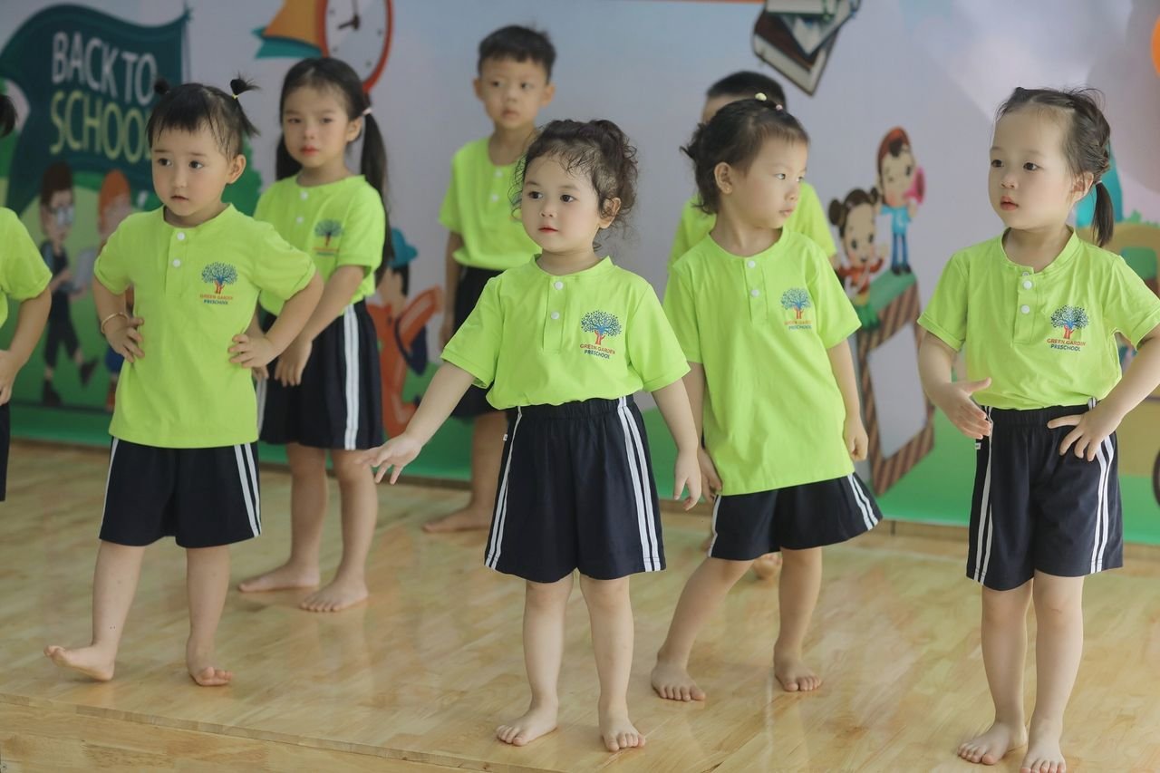 Young children participate in a fun dance class, dressed in green and black uniforms at a Vietnamese preschool.