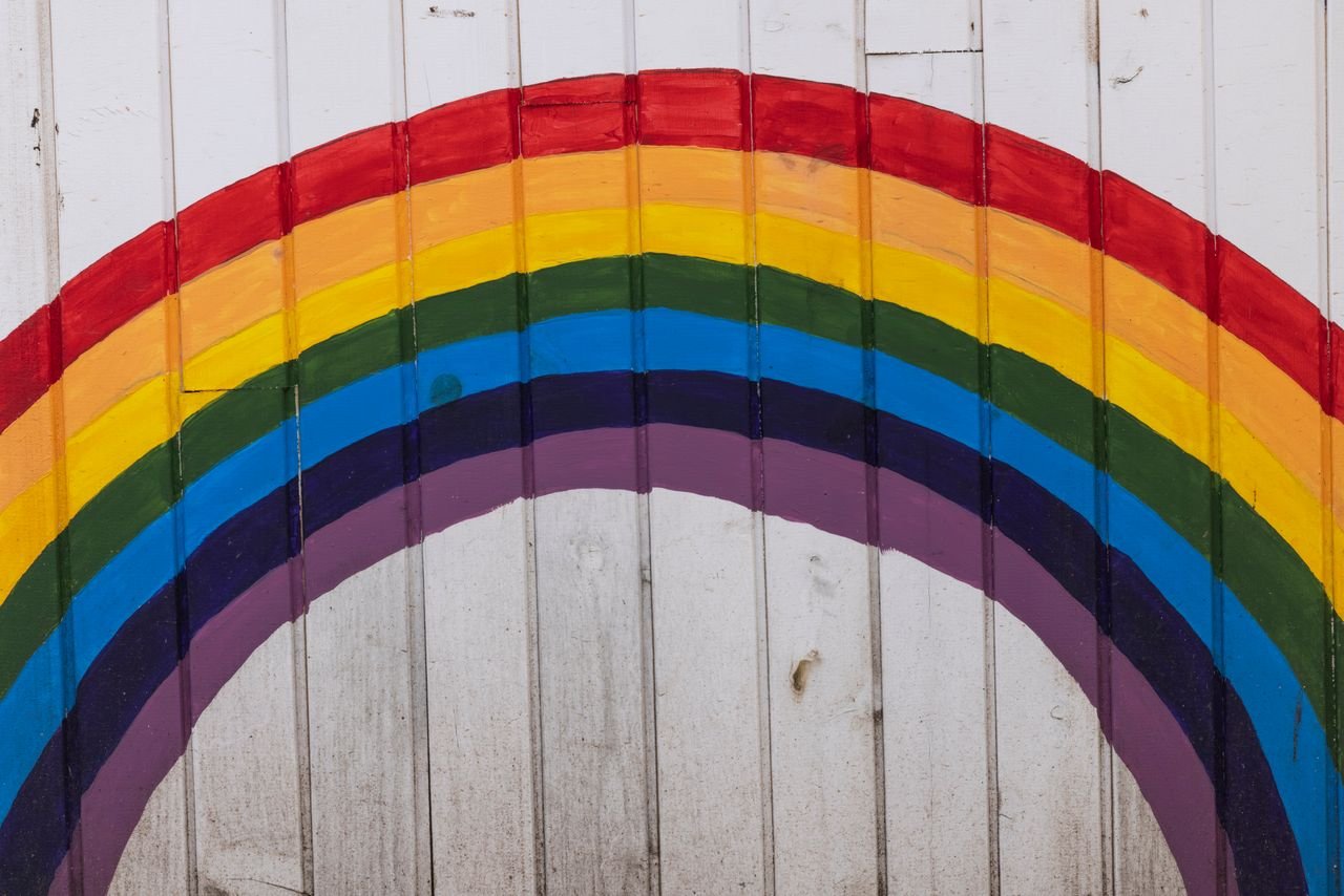 Vibrant rainbow painted on a white wooden wall, symbolizing hope and diversity.